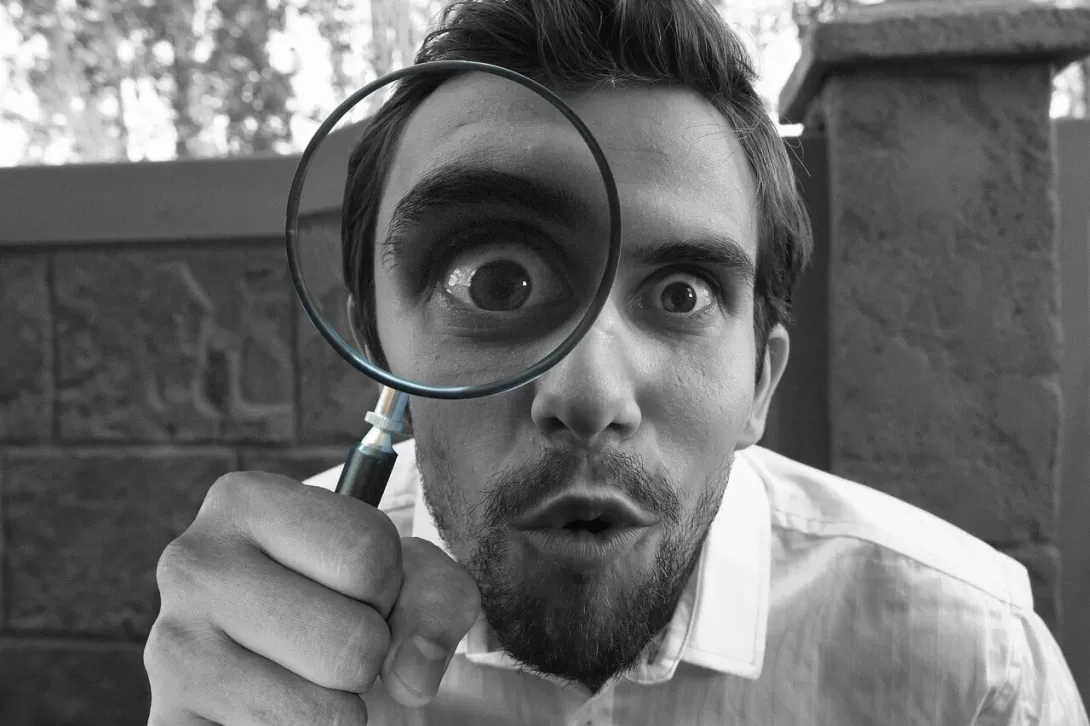 A man looking into the camera with a magnifying glass 